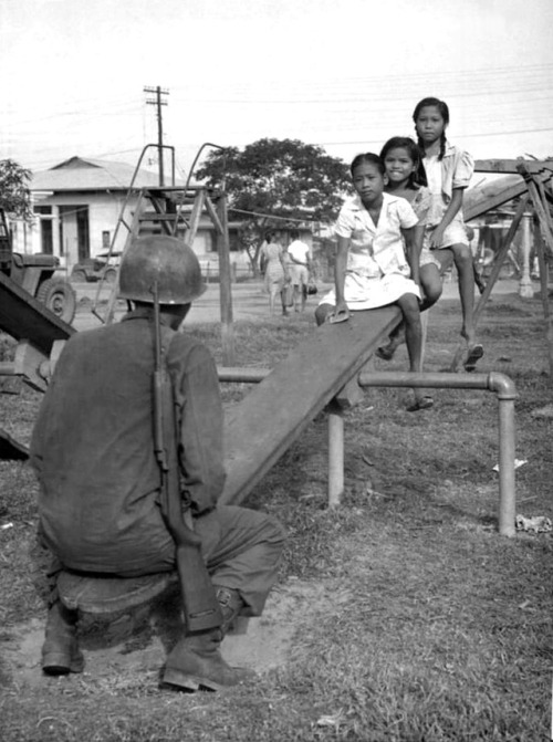 A U.S. Army soldier plays see-saw with young Filipino girls following the Allied amphibious landings