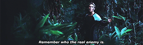 An animated gif from The Hunger Games - a man stands in a jungle at night calling back towards the camera, "remember who the enemy is"