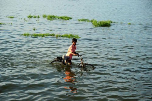 A villager pushes a bicycle as he crosses a flooded road at Naraha on the outskirts of Allahabad on 