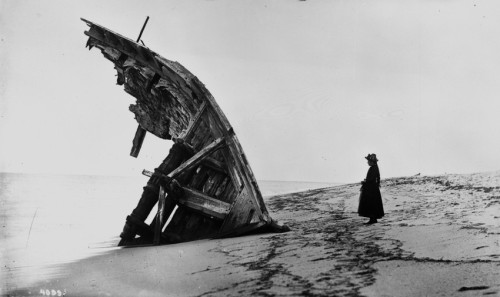 beggars-opera:A woman stands next to the remains of the hull of the Warren Sawyer on the beach at Su