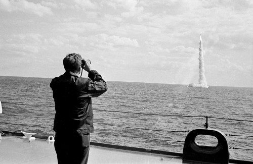 President John F. Kennedy watches through binoculars as a Polarismissile clears the surface after fi