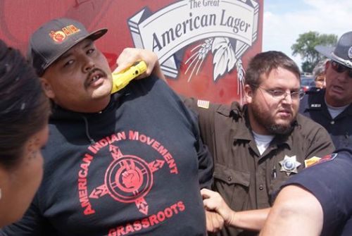 fuck-the-conquistadores:  katfiercefeather:  his-name-is-nightrider:  ‘”This cop is holding a taser to the neck of a Lakota man blocking the passage of a beer truck in White Clay, Nebraska. Despite police violence, the action was a success - two Budweiser