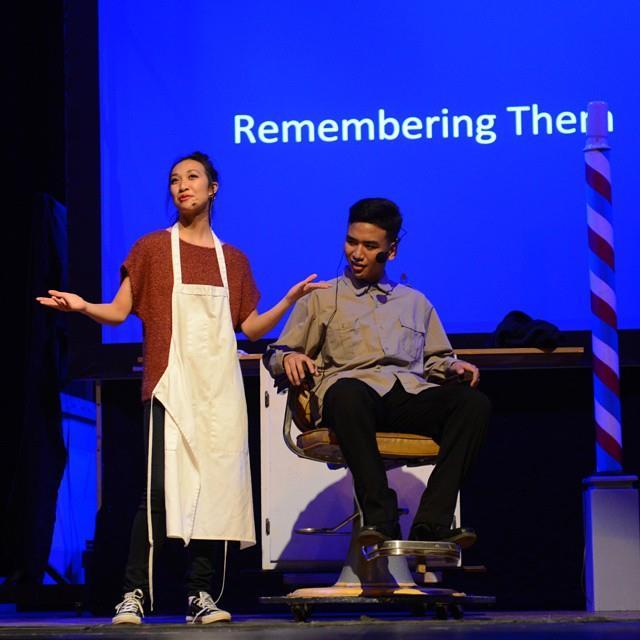 A photo of a female actor wearing a barber's apron and a male  actor sitting in a barber's chair in a short play titled, REMEMBERING THEM, about the power an old barber shop chair to bring back the memories of the manongs who sat in it.