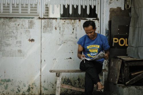 Man reads newspaper. A police riot shield is partially hidden behind him.Bandung, Indonesia
