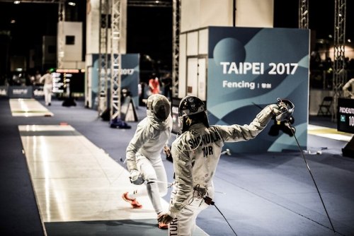 [ID: a sabre fencer just after making a skyhook, her opponent in mid-step.]Fencing at the 2017 Summe