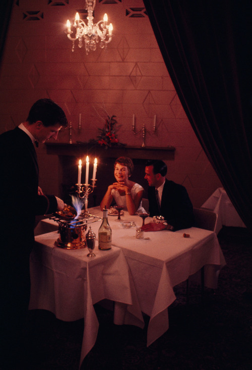 A couple watches a waiter prepare a flaming fruit dessert in New Zealand, 1962. Photograph by Robert