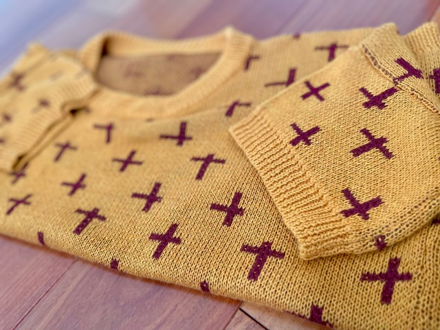 A short sleeved, yellow knit sweater, folded on a wooden floor.