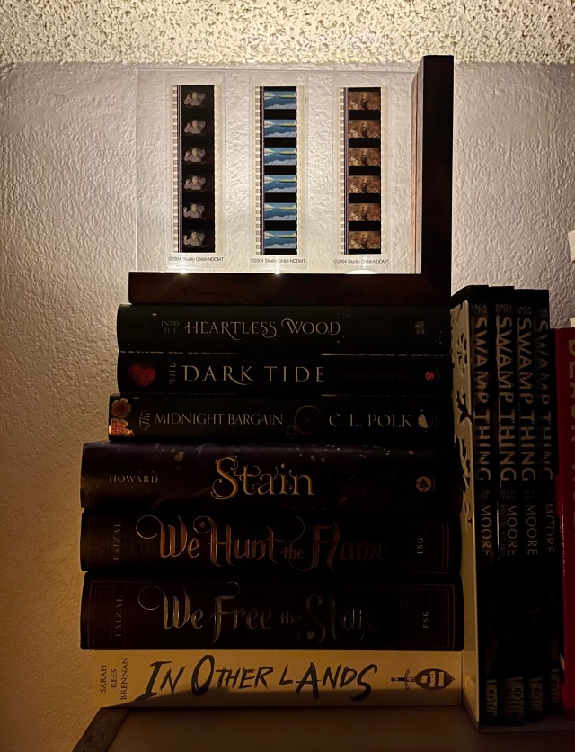 a stack of books with a picture frame on top. the picture frame holds 3 fild strips from Howls movie castle