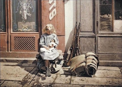 A little girl playing with her doll in Reims (France, 1917).  Two guns and a knapsack are next to he