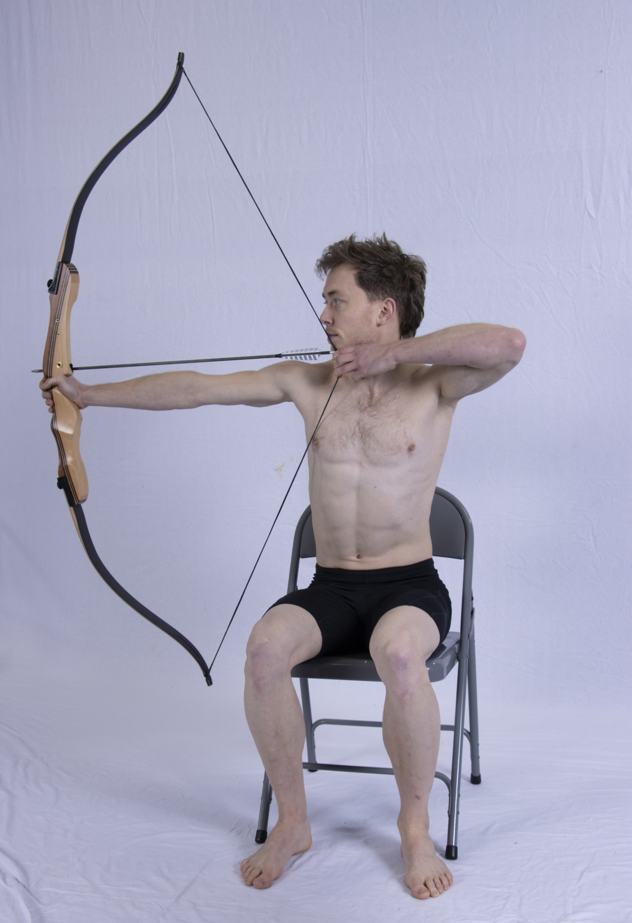 A photograph of a man shooting a bow from a seated position