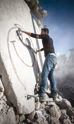 vicemag:  Khalifa, a graffiti artist in Aleppo, Syria, sprays a smiley face onto the wall of a building destroyed by a Scud missile 