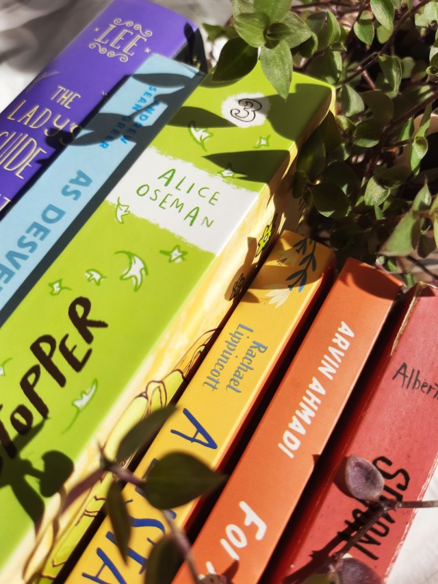 a close-up of the spines of the books with some vines of the plants over them. 