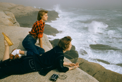 natgeofound - Two women gaze at heavy surf while lying on boulders...