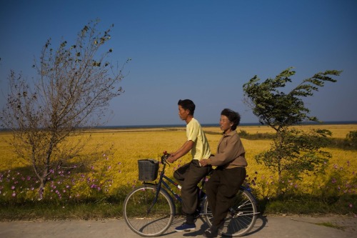 A couple on a bicycle coast down a hill past farm fields outside the eastern coastal city of Wonsan,