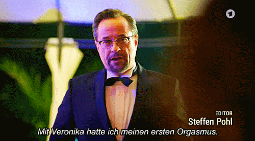 Boerne hält eine Rede und lächelt jemanden im Publikum an. Er sagt: "Mit Veronika hatte ich meinen ersten Orgasmus."