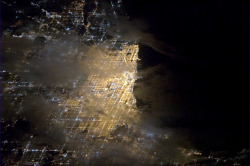 colchrishadfield:  Chicago, a bright spot on the tip of Lake Michigan, glowing through the clouds. 