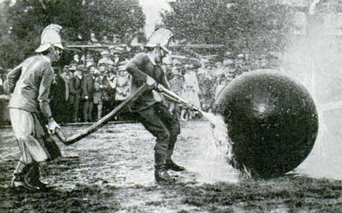 An exciting moment in the game of firemen’s pushball. With spray flying in all directions, the players are taking the ball down the field for a try at their opponents’ goal, 1922.