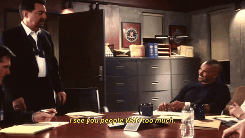 Rossi speaks, bringing his hands slightly towards himself and then out for emphasis, raising one brow and widening one eye as he does. He sits. Morgan and Garcia watch him, still smiling. Yellow subtitles read: "I see you people way too much." The word "way" is in all caps.