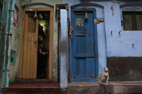 A Bangladeshi woman cleans the doorway to her home as a cat sits nearby early in the morning in Dhak