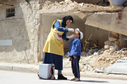A health worker vaccinates a young child against polio in the Sakhour neighborhood of Aleppo, Syria,