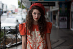 lordeella-style:  Lorde wearing a Orange glow-in-the-dark dress by Karen Walker, beanie and matching lipstick. With her distressed brown leather vintage bag and Doc Marten shoes.  