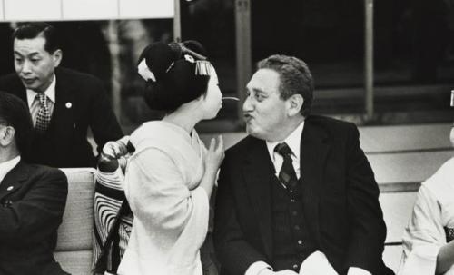 American Secretary of State Henry Kissinger plays a “pass the straw” game with a woman dressed as a 