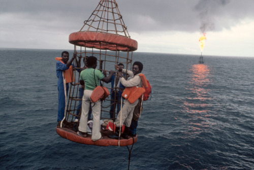 unrar:   Workers are hoisted aboard an offshore oil rig at the ELF Company’s Grandin complex in Gabon, 1984,  Bruno Barbey.