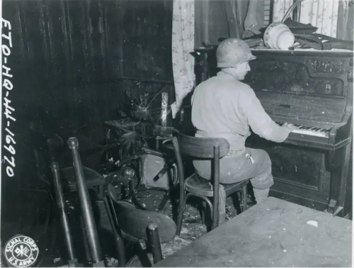 A US Soldier From The 119th Infantry Regiment Relaxes By Playing Piano In A Wrecked Beer Hall In Bach,