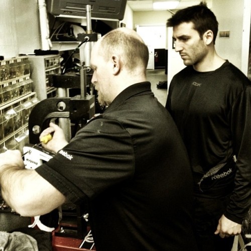 Bergeron looks on as equipment manager Keith Robinson works on his skates before practice. #BruinsAreBack