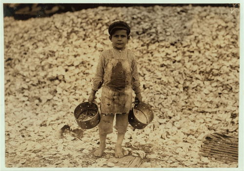 Original Caption: Manuel, the young shrimp-picker, five years old, and a mountain of child-labor oys