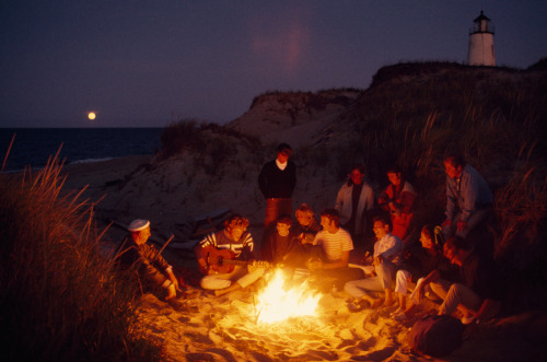 Friends gather around a summer campfire at Great Point Lighthouse on Nantucket Island, Massachusetts