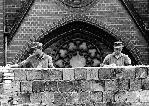 Two East German workers placing pieces of broken glass on top of the Berlin Wall (1961).