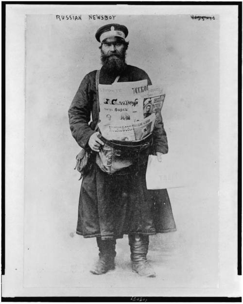 Russian newspaper delivery man with bundle of newspapers (1900 - 1918).