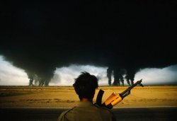 historicaltimes:  An Iranian soldier looks out over the desert, darkened under clouds of burning oil set alight by Iraqi forces in 1990. 