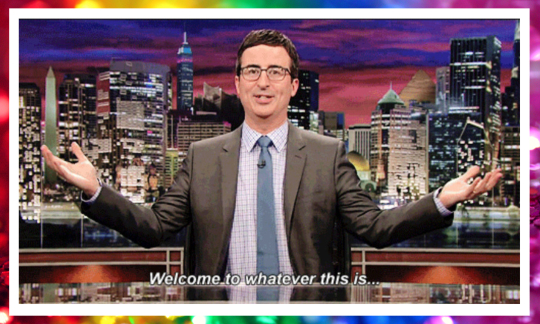 ID: a picture of TV presenter John Oliver holding his arms wide with a sardonic expression saying, “Welcome to whatever this is...”  The image is surrounded by a gradient rainbow frame.