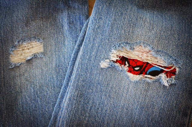 Spiderman peaking out of a rip in a pair of blue jeans.