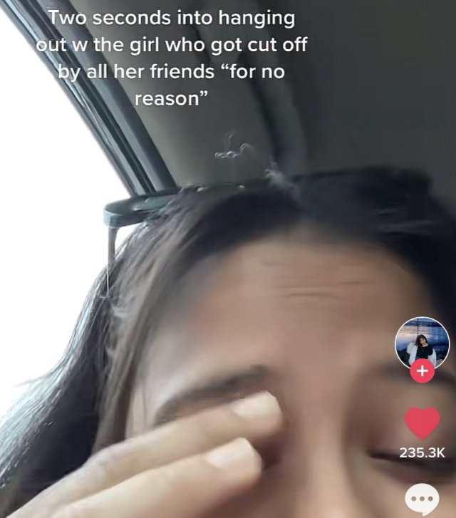 cropped screenshot of a tiktok with the caption "two seconds into hanging out with the girl who got cut off by all her friends 'for no reason'". the cropped image is of a person with their eyes closed rubbing a hand over their brow. they seem resigned. 