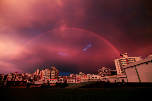 sixpenceee:    A rainbow appears in the sky as lightning strikes during a rainstorm on May 13, 2012 in Haikou, China. Photo credit: China Foto 