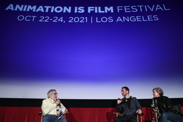 Photos by John Salangsang 2021, director and translater sit at right across from interviewer in front of the large movie screen that reads Animation is Film Festival 2021