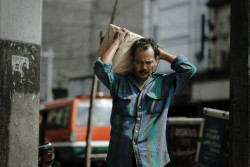 Man looks on as he carries a box. Bandung, Indonesia