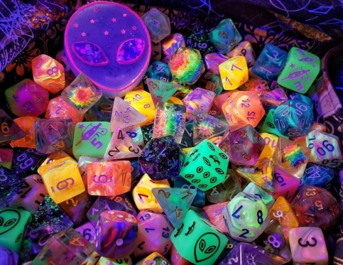 polyhedral-amorous: [Image description: Dice of every shape and color are glowing under a black ligh