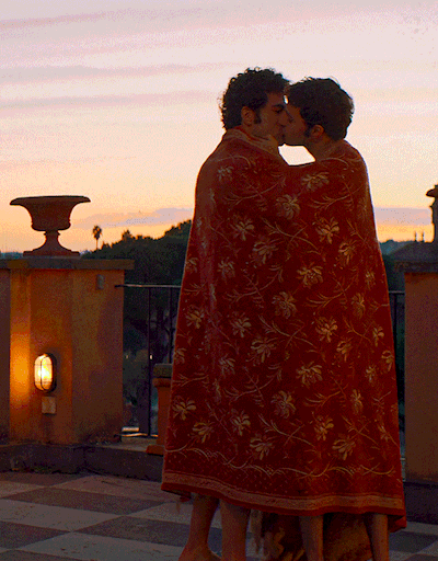Pietro &  Enea kiss in embrace on a rooftop with sweeping views of the roman city skyline at sunrise. The red & gold hand embroidered area rag doubling as blanket around them falls off revealing Enea's posterior. 

Nuovo Olimpo (2023) · Romance · dir. Ferzan Özpetek

 · [Gif Creator/Editor: k-wame.tumblr.com]