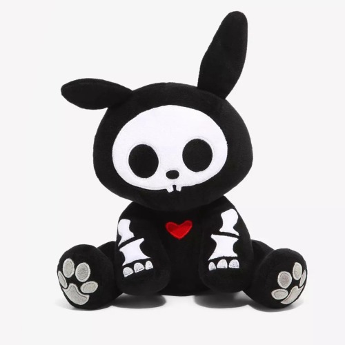 A stuffed animal of a black bunny with a white skeleton. The bones are cartoony and simple. There is a small red heart in the middle of its chest.