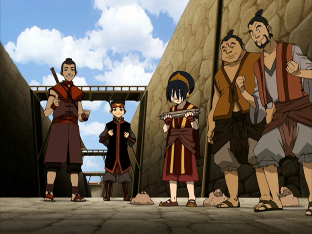 toph holding two things that look like sticks. sokka and aang to her left. two men to her right looking very excited. 