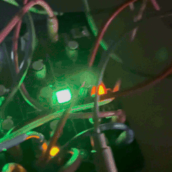 a modular synth setup, several rectangular electrical panels connected together by a dense tangle of wires to produce music. small lights across the synths can be seen blinking green and orange