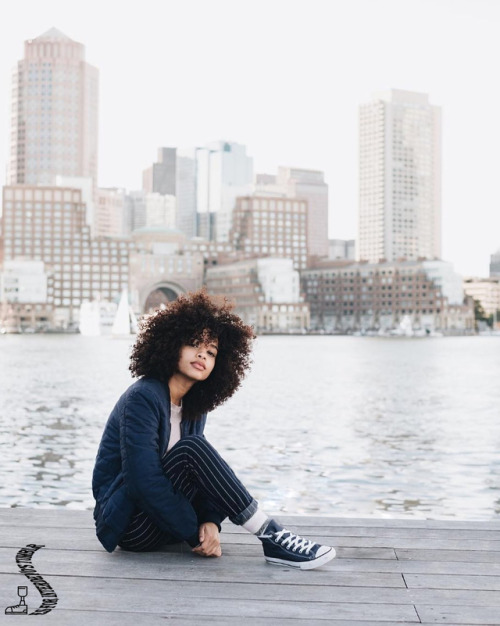 interdevo: a lush-haired girl in black striped trousers and black classic converse sneaker sits on t