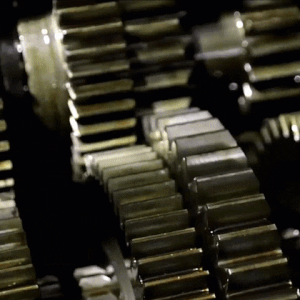 a gif. old, oily gears in a machine move in bursts.