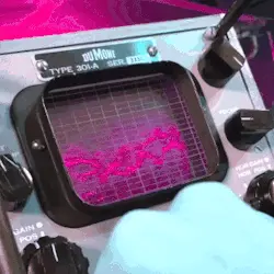 a person adjusting a dial on an old oscilloscope with a green display. lines jump across the display erratically.