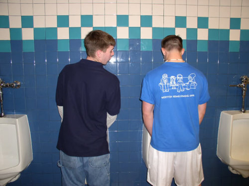 Sneaking a peak at his buddy, while taking a leak in the urinal.