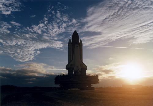 The rising sun and some scattered clouds provide a picturesque backdrop for the Space Shuttle Discov